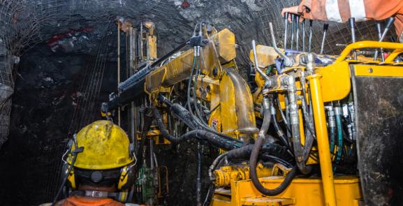 workers wearing safety clothing and helmets working with machiney in a mine